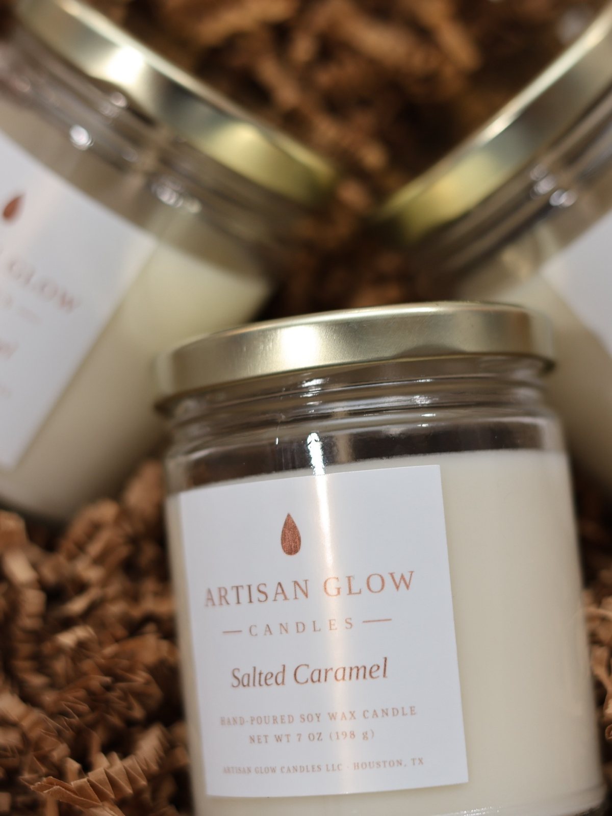 Three Salted Caramel soy candles with gold lids resting in kraft crinkle paper